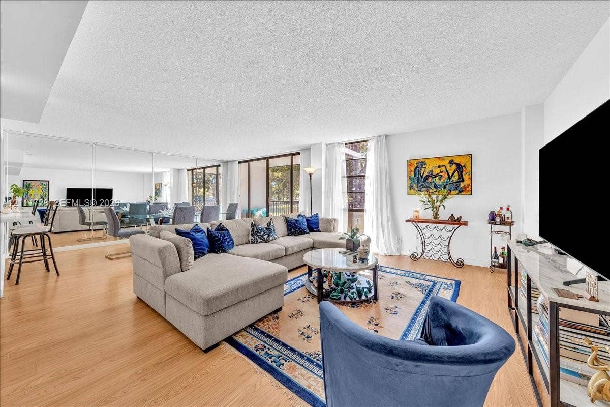Open-concept living area featuring wood-finish flooring, floor-to-ceiling mirrored wall paneling, and sliding glass door access to a private balcony
