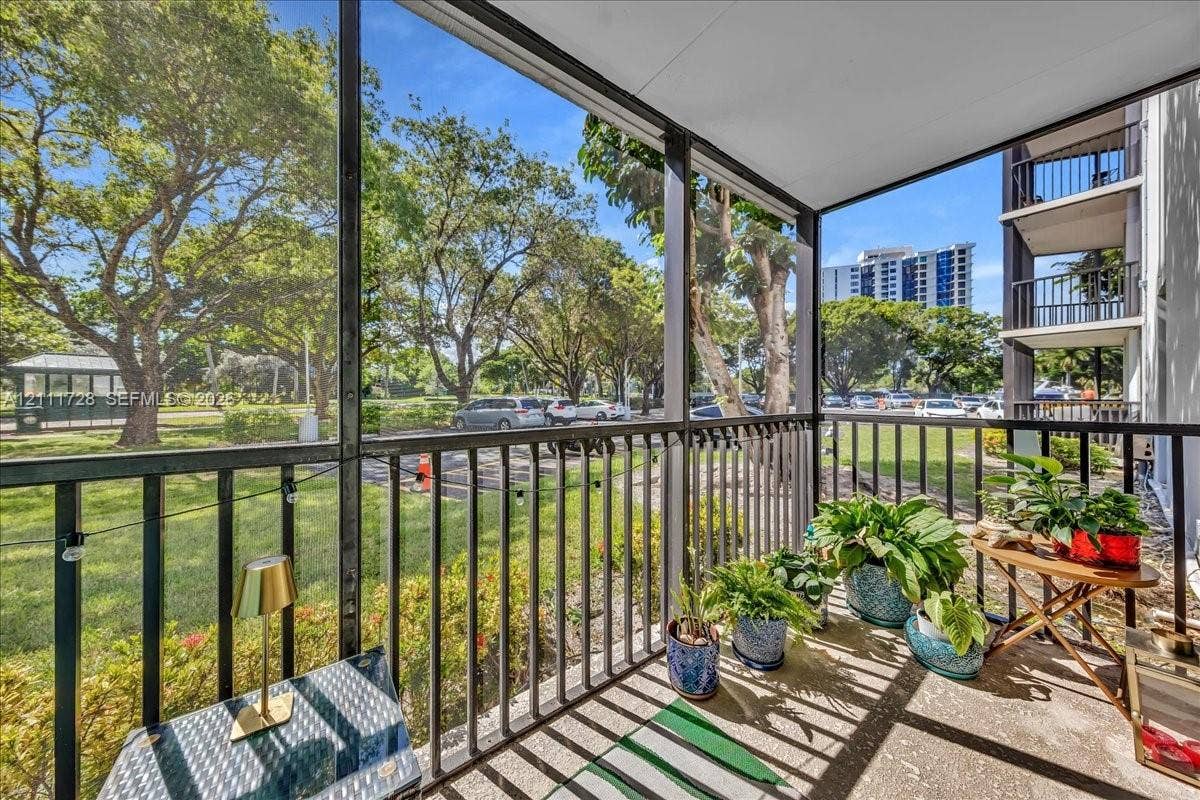 Screened-in balcony featuring metal railings, concrete flooring, and mature tree-lined landscaping
