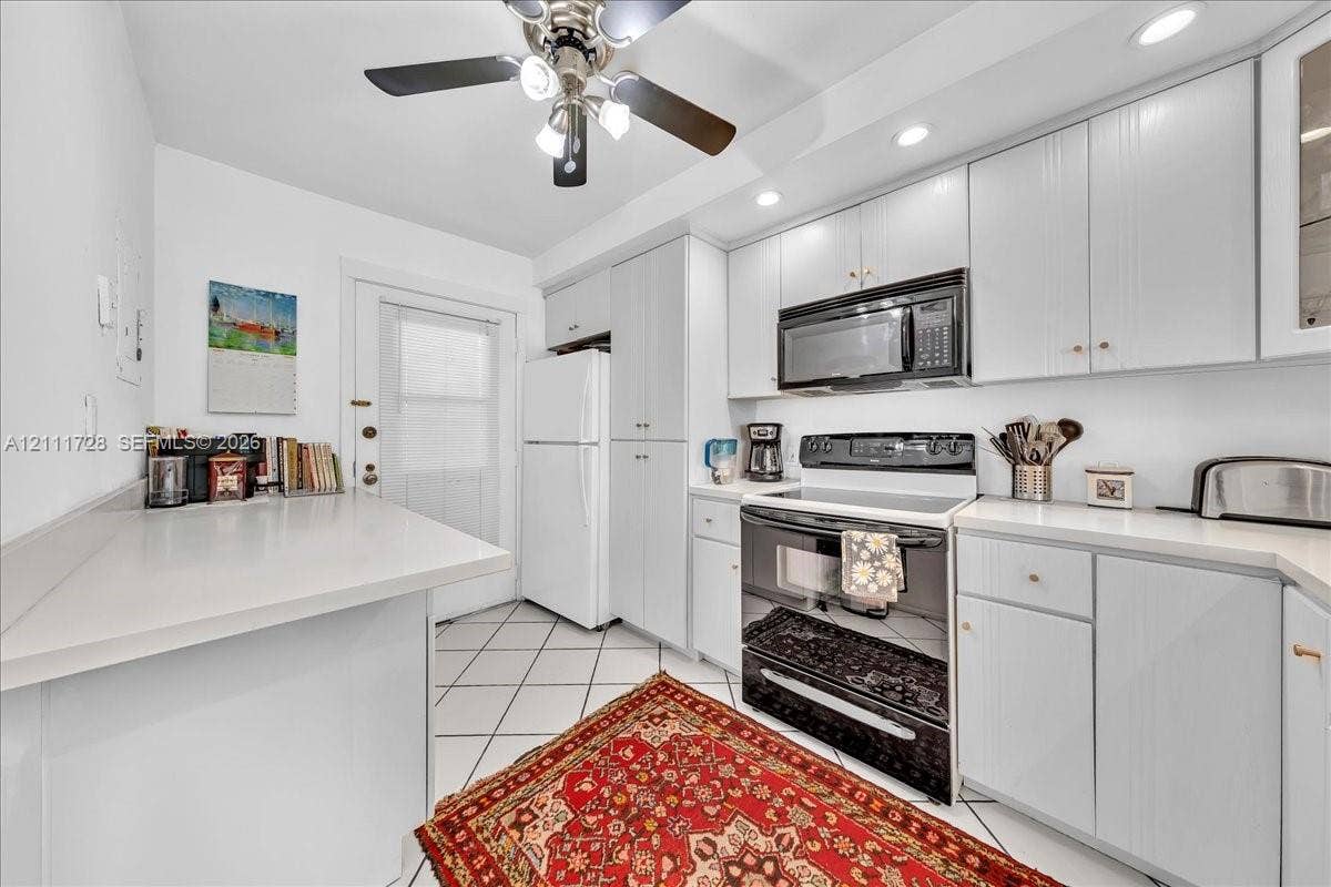 Kitchen featuring white cabinetry, solid-surface countertops, black finish range and built-in microwave, ceiling fan with integrated lighting, and tile flooring