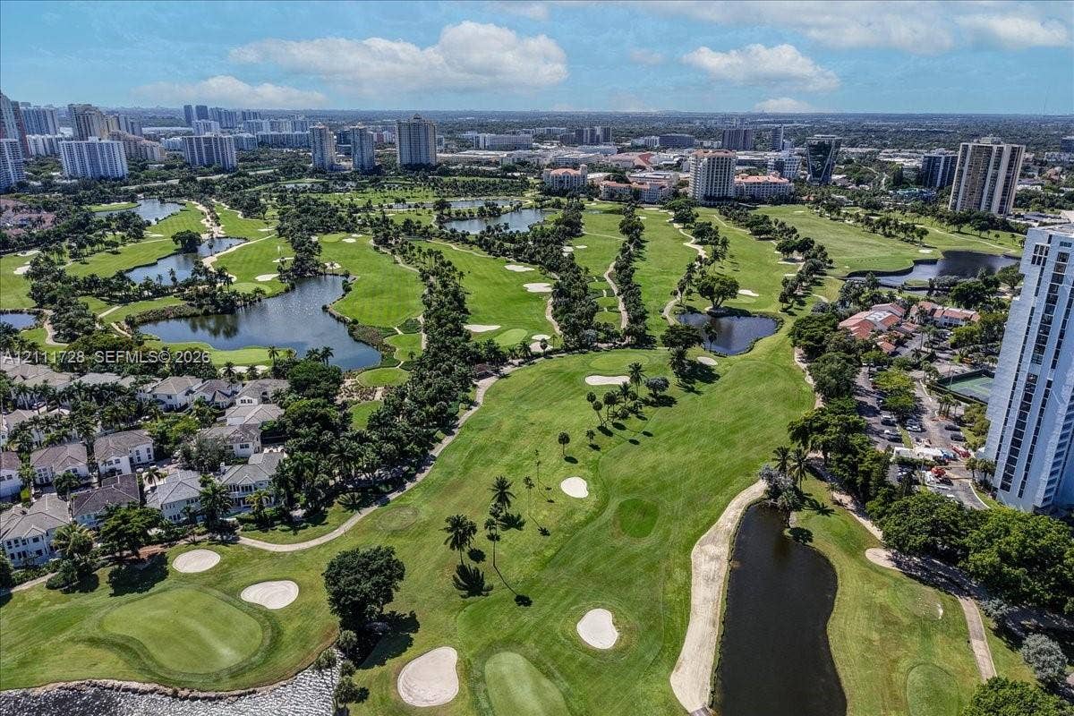 Aerial perspective of a golf course featuring expansive green fairways, multiple water hazards, sand bunkers, and mature palms