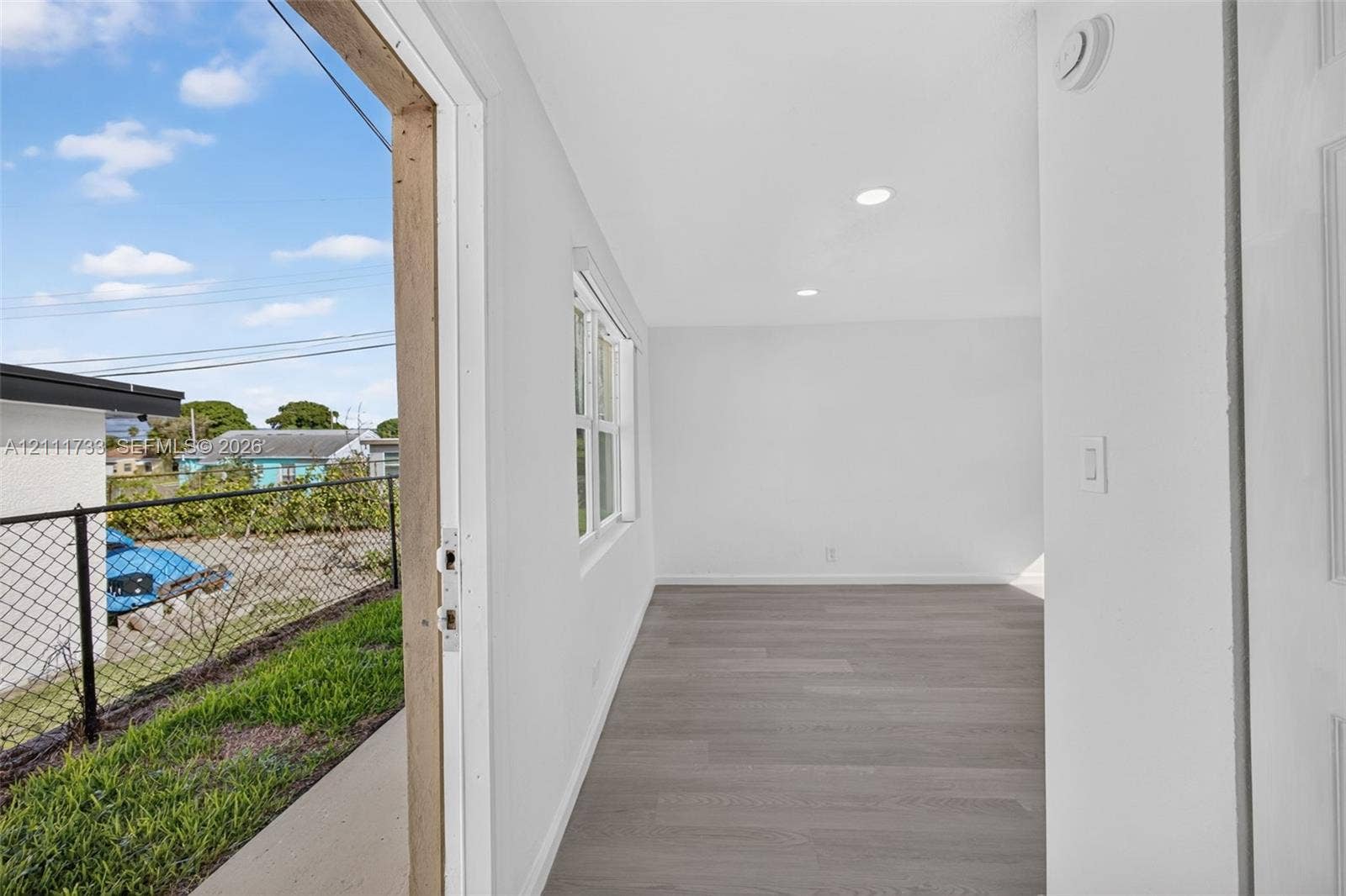 Interior view from front area thru door (lock-off) to rear bedroom and showing open rear exterior entry door to left. featuring wood-finish flooring, recessed lighting, and a multi-pane window