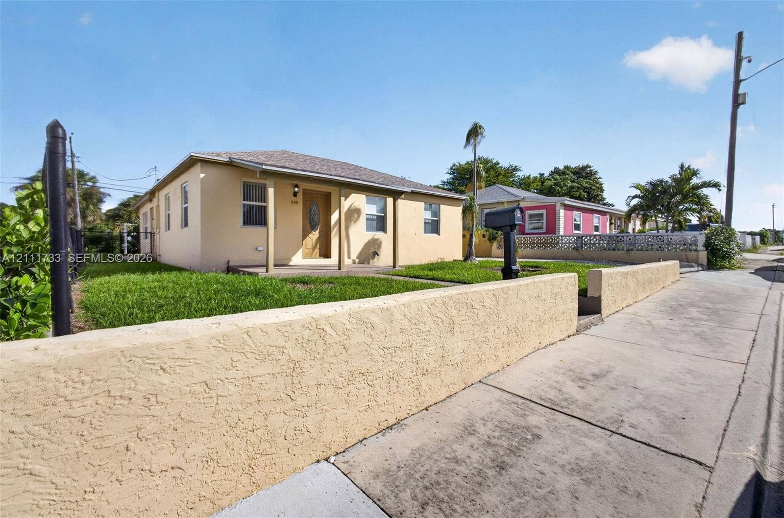Single-story stucco exterior featuring a covered front porch, low-profile masonry perimeter wall, and manicured lawn