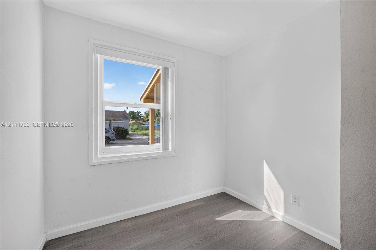 Front bedroom featuring white-painted walls and wood-finish flooring with an inset double-hung window