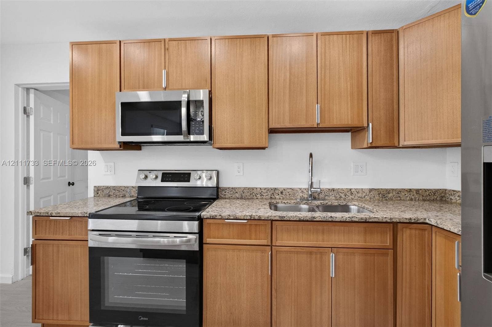 Kitchen featuring wood-finish cabinetry, stone-patterned countertops, a stainless steel electric range, an over-the-range microwave, and a dual-basin sink with a chrome faucet