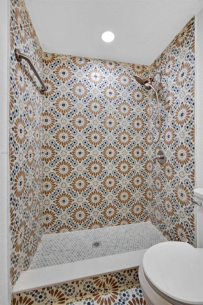 Walk-in shower featuring patterned tile walls, hexagonal floor tile, a ceiling-mounted light fixture, and a handheld showerhead