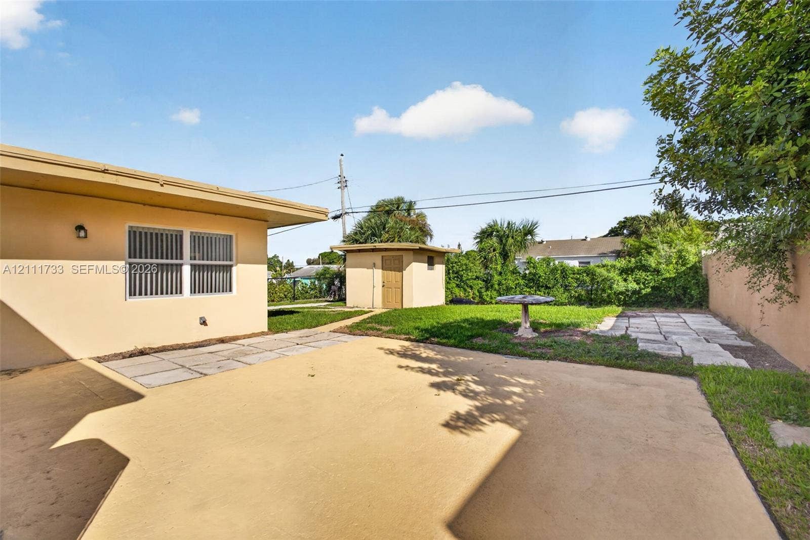 Rear exterior space featuring a concrete patio, a detached shed with laundry room, stone paver accents, and a grass lawn area.