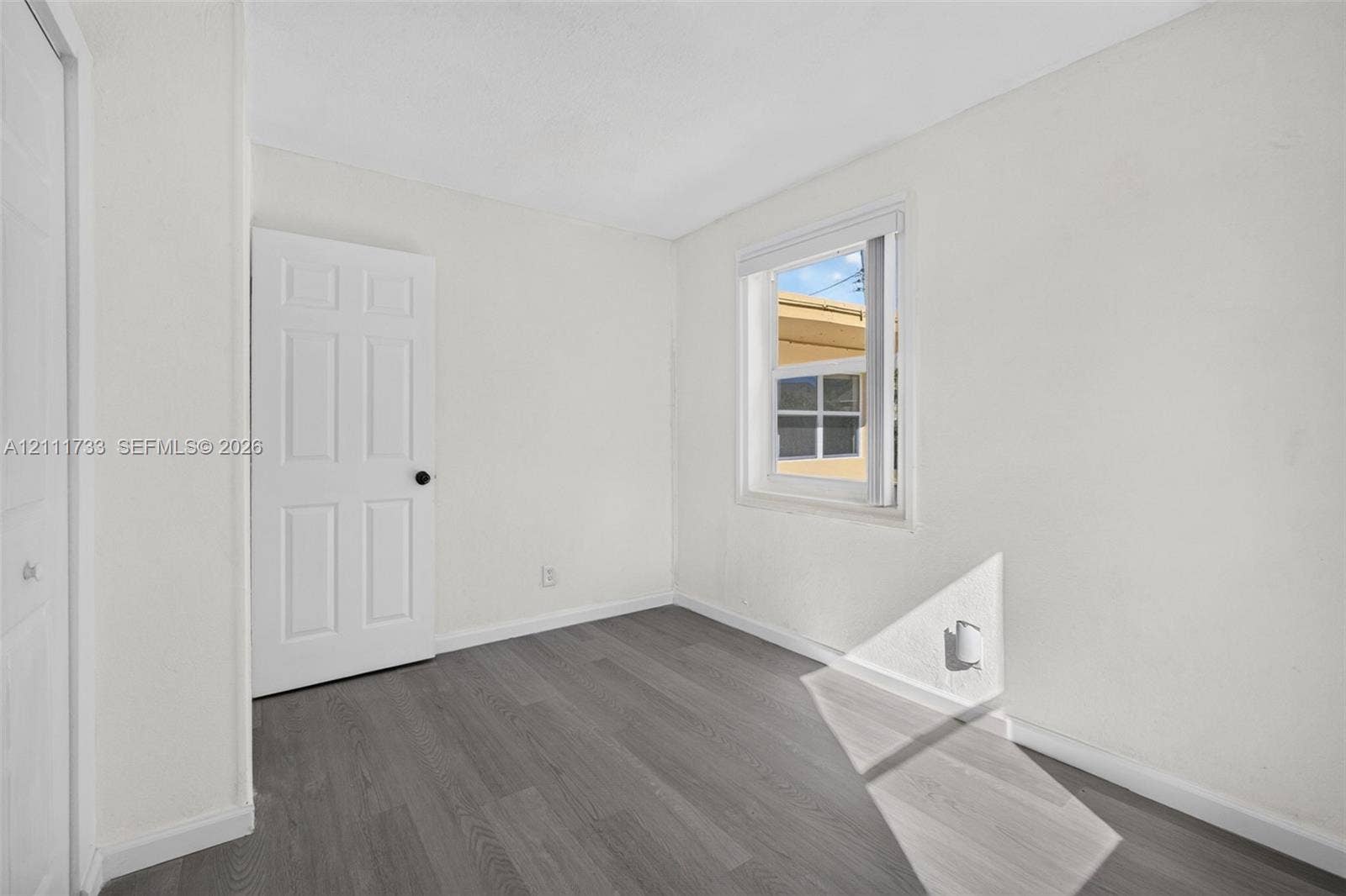 Front bedroom viewfeaturing wood-finish flooring, a single-panel interior door, and a white-framed window