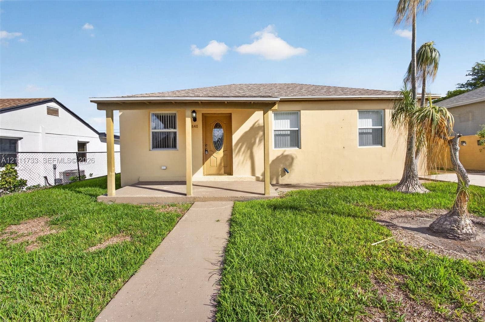 Single-story exterior featuring a covered front porch, stucco facade, hipped roofline, and palm trees