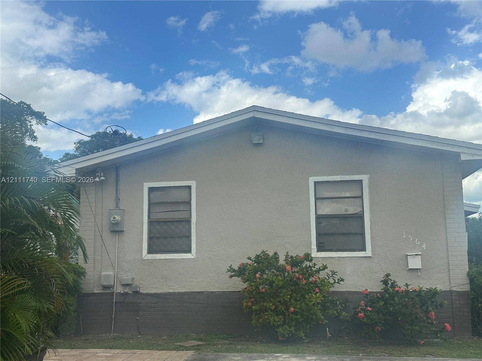Stucco exterior featuring two single-hung windows, a gable roofline, and established landscaping