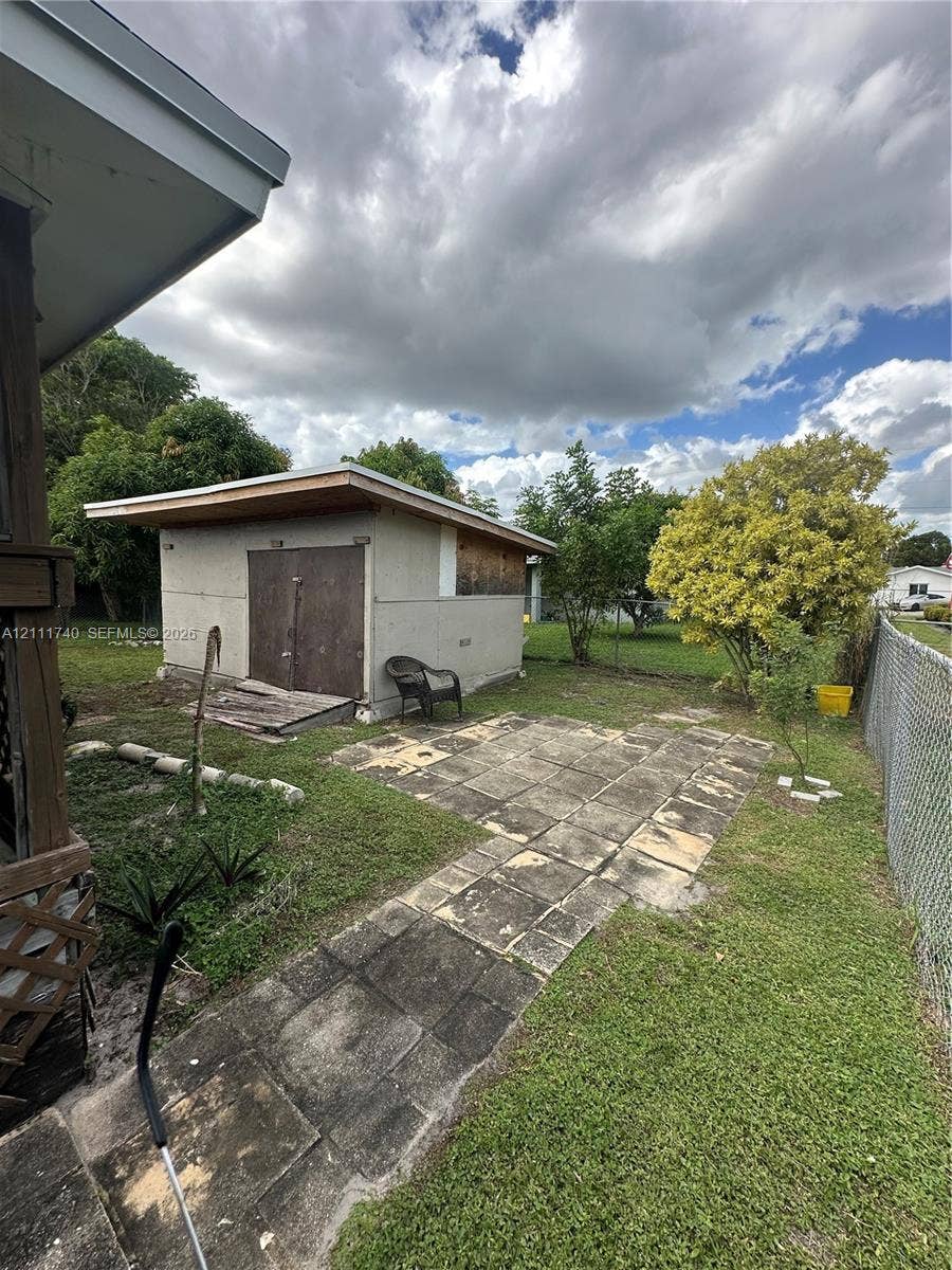 Exterior storage structure with a shed roof, paved stone patio, and chain-link fencing