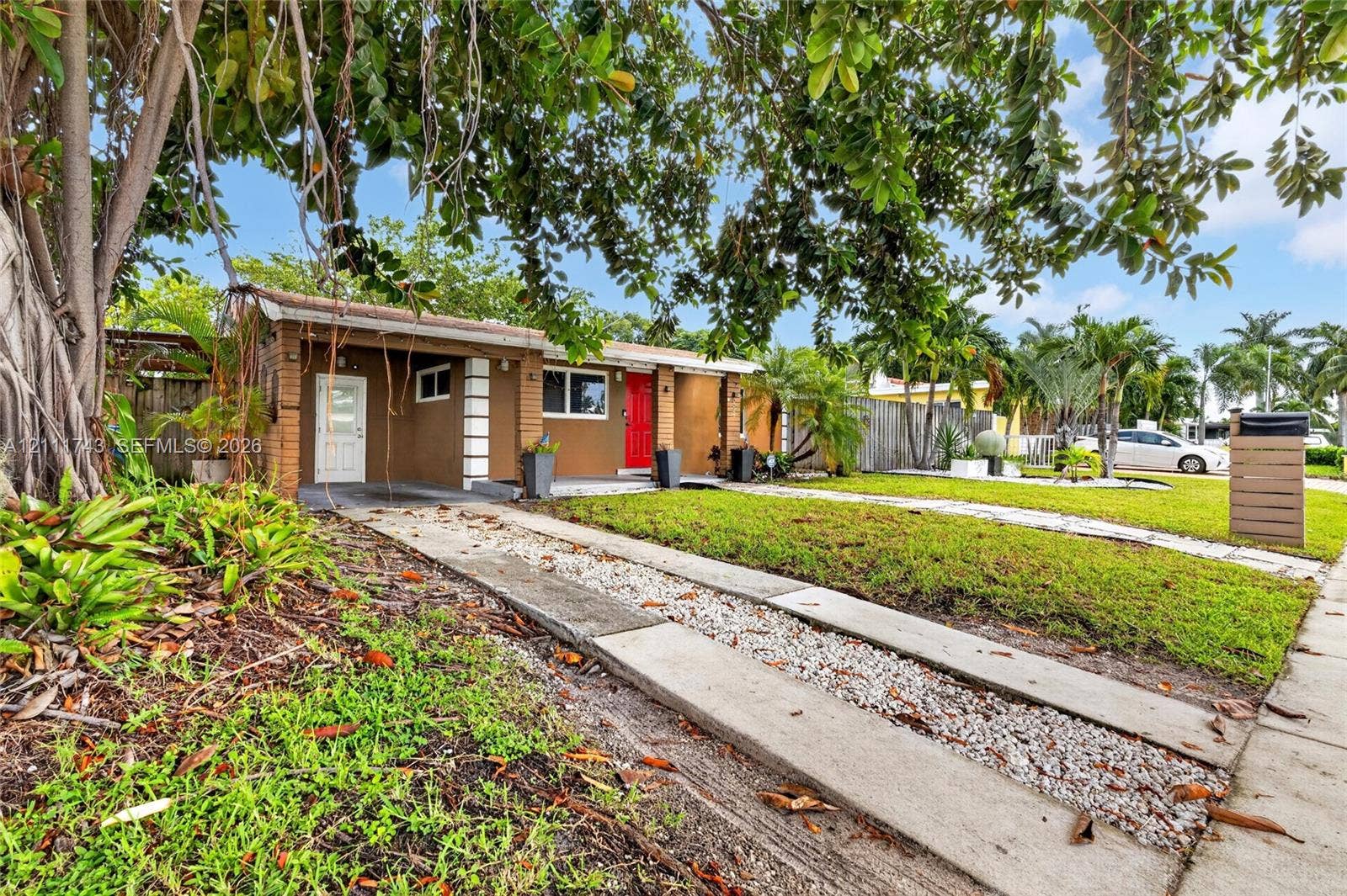 5524 N Andrews Avenue, Oakland Park, FL 33309 Single-story exterior featuring a brown stucco facade, brick-accented columns, a paved concrete driveway with aggregate detailing, and mature perimeter landscaping