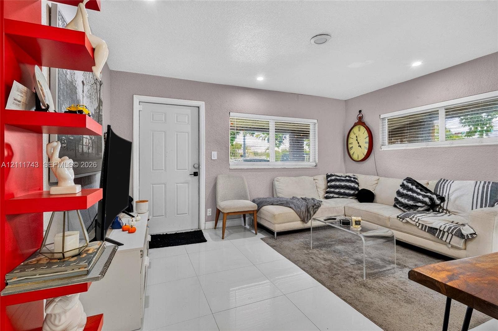 5524 N Andrews Avenue, Oakland Park, FL 33309 Bright living area featuring glossy large-format floor tiles, recessed lighting, double-pane windows, and a built-in floor-to-ceiling shelving unit