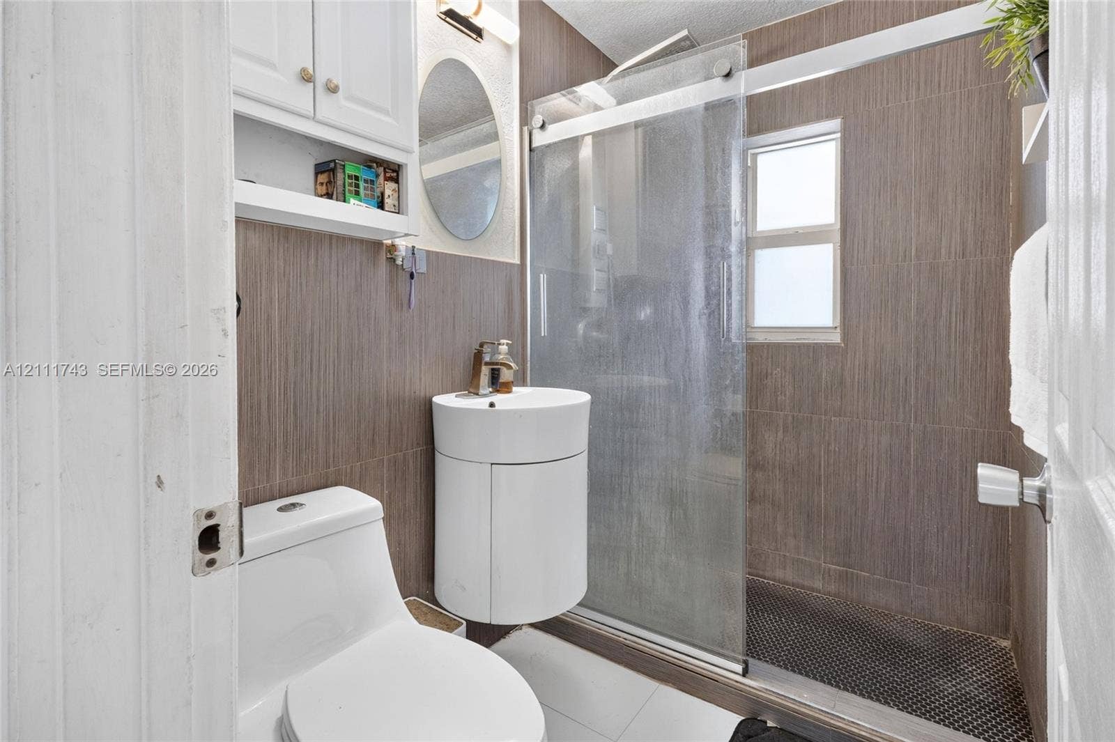5524 N Andrews Avenue, Oakland Park, FL 33309 Bathroom featuring wall-to-wall vertical tile, sliding glass shower door, corner-mounted vanity with integrated sink, and white wall-mounted cabinetry