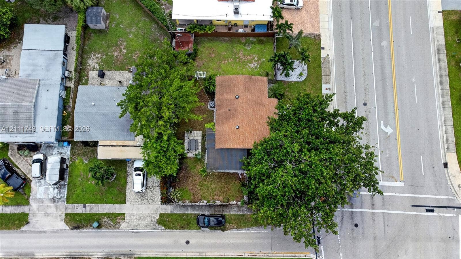 5524 N Andrews Avenue, Oakland Park, FL 33309 Aerial perspective of residential property featuring a shingle roof, mature landscaping, paved driveway, and grass lawn area