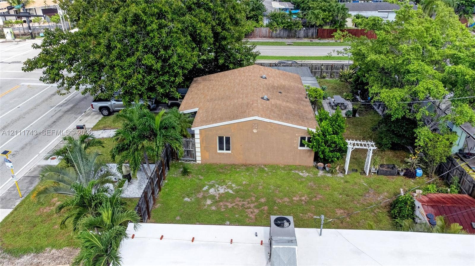 5524 N Andrews Avenue, Oakland Park, FL 33309 Exterior of a single-story structure featuring a pitched shingle roof, stucco facade, decorative trellis, and mature landscaping
