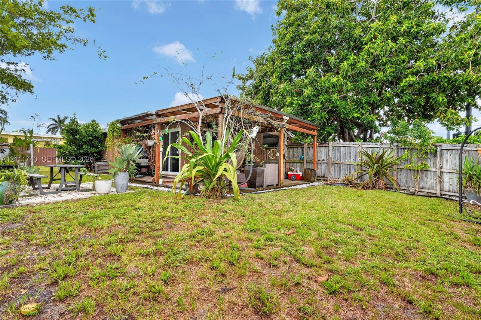 5524 N Andrews Avenue, Oakland Park, FL 33309 Rear exterior featuring a wood-frame pergola, concrete paver accents, and wood-panel privacy fencing