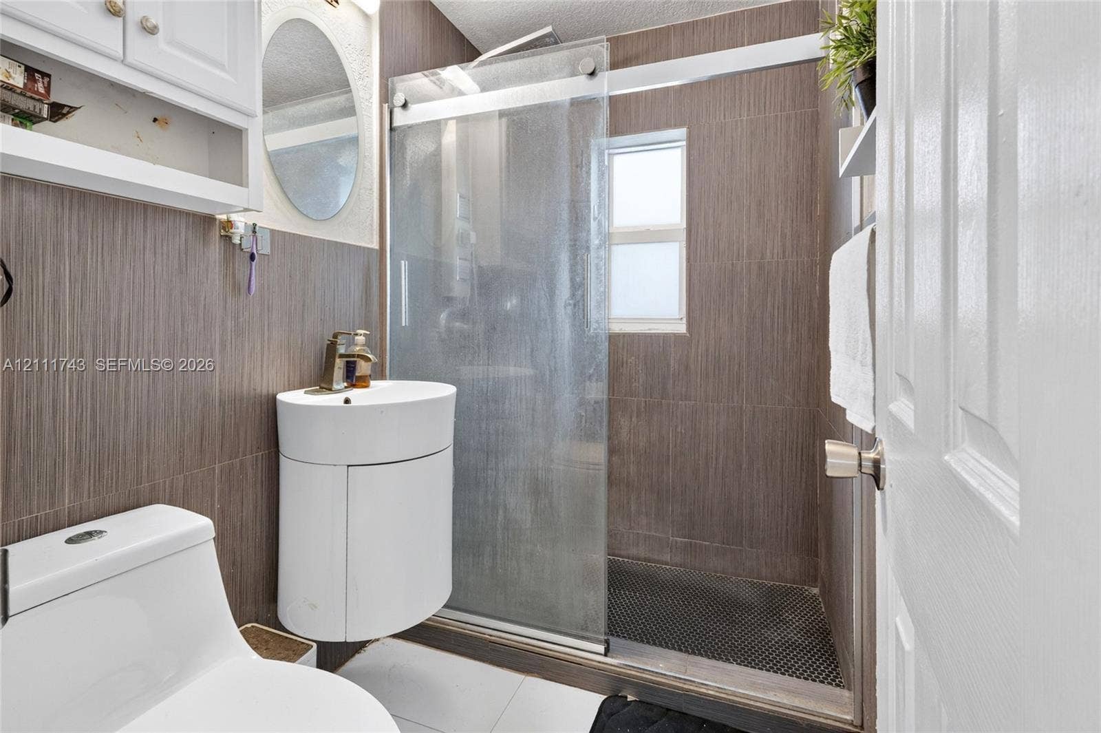 5524 N Andrews Avenue, Oakland Park, FL 33309 Bathroom featuring vertical wood-finish wall tile, a semi-circular pedestal sink with a metallic faucet, and a shower enclosure with a glass sliding door
