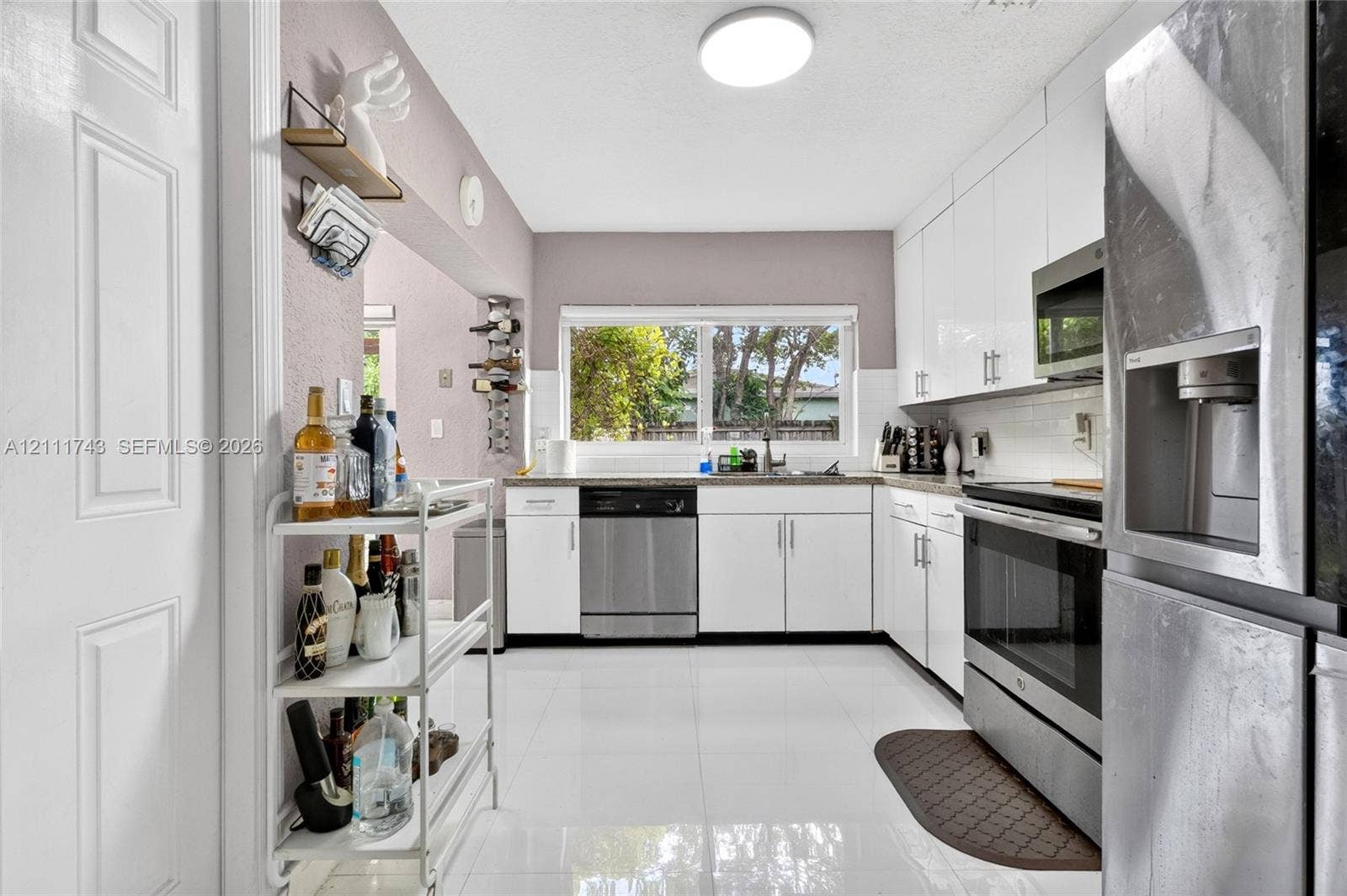 5524 N Andrews Avenue, Oakland Park, FL 33309 Kitchen featuring high-gloss white cabinetry, stainless steel appliances, white tile flooring, white subway tile backsplash, and a large horizontal window