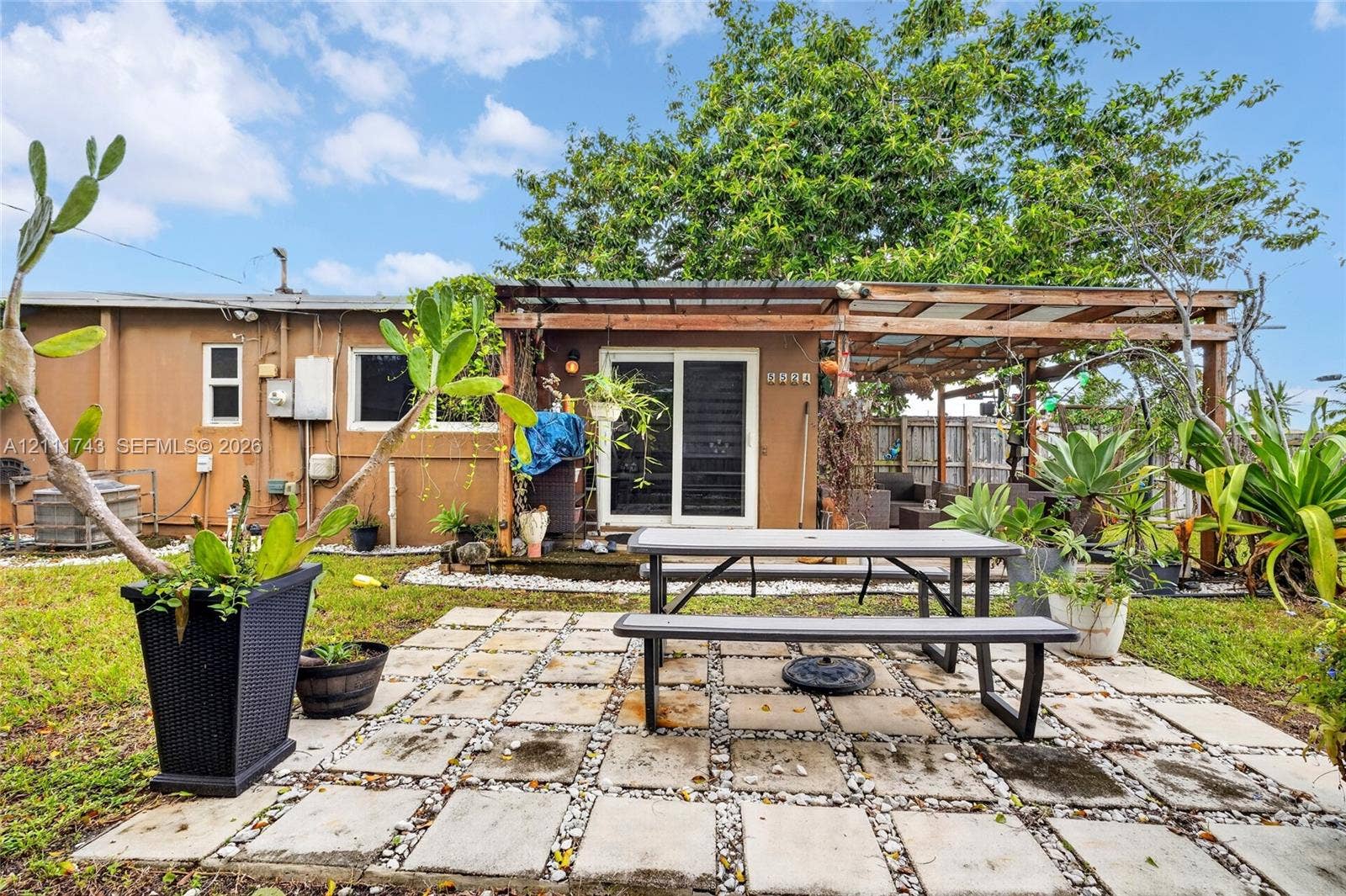 5524 N Andrews Avenue, Oakland Park, FL 33309 Rear exterior space featuring a square-paver patio, a wooden pergola structure, sliding glass doors, and mature landscaping