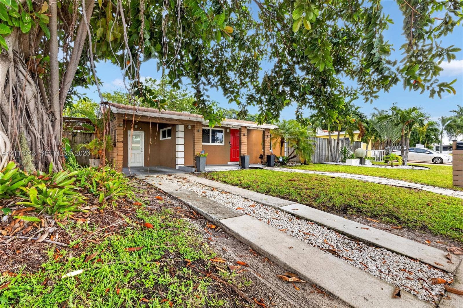 5524 N Andrews Avenue, Oakland Park, FL 33309 Single-story residence featuring a brick exterior, stone-inlay driveway, covered entrance, and mature landscaping