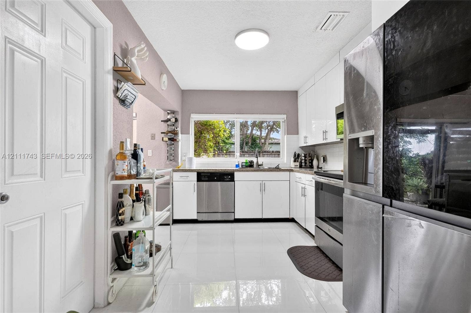 5524 N Andrews Avenue, Oakland Park, FL 33309 Kitchen featuring white flat-panel cabinetry, stainless steel appliances, polished tile flooring, and a window over the sink