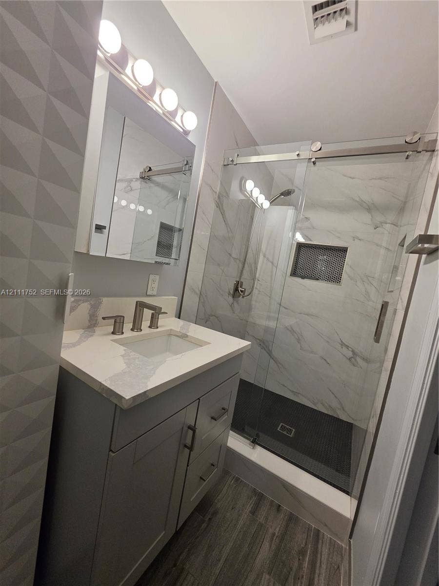 2901 NE 11th Terrace, Pompano Beach, Pompano Beach, FL 33064 Bathroom featuring a vanity with a quartz countertop and integrated sink, a glass-enclosed shower with tiled walls and built-in niche, and wood-finish flooring
