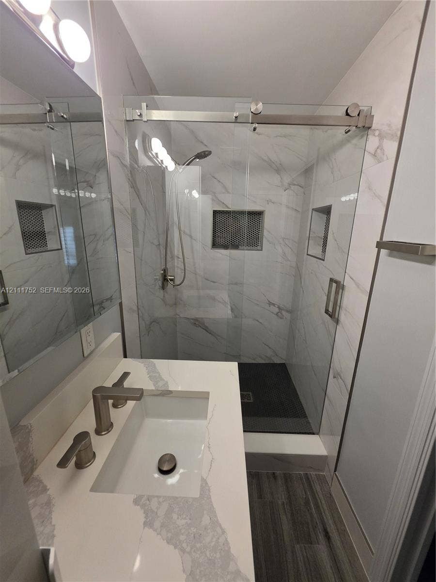 2901 NE 11th Terrace, Pompano Beach, Pompano Beach, FL 33064 Bathroom featuring a vanity with a stone-finish countertop, walk-in shower with sliding glass doors, floor-to-ceiling tile work, and recessed wall niches