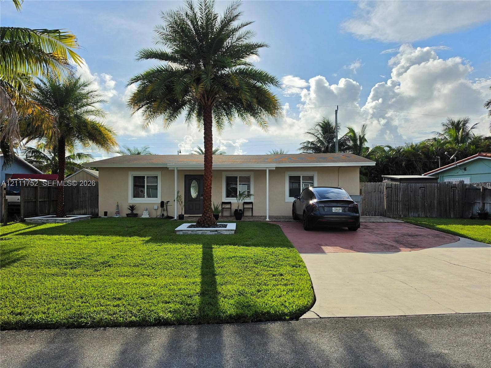 2901 NE 11th Terrace, Pompano Beach, Pompano Beach, FL 33064 Single-story residence featuring a stucco exterior, concrete driveway, front yard landscaping, and mature palm trees enclosed by wooden perimeter fencing
