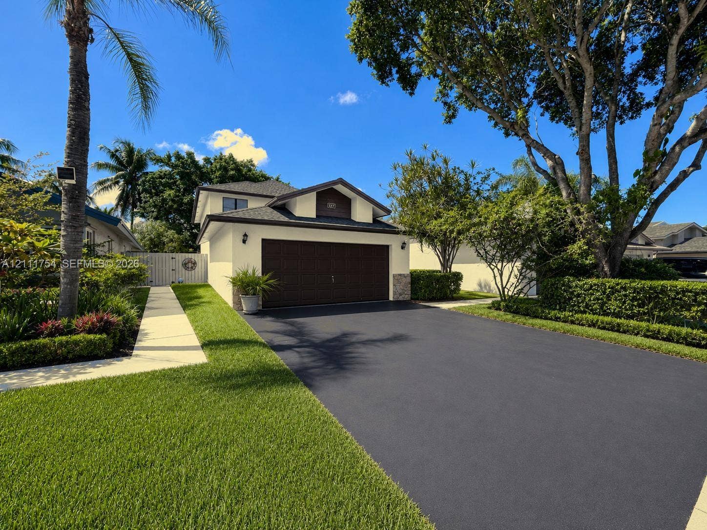 527 Lakeside Circle, Sunrise, FL 33326 Exterior featuring a gabled roofline, concrete driveway, two-car garage with dark-finish door, stone-accented facade, and manicured landscaping