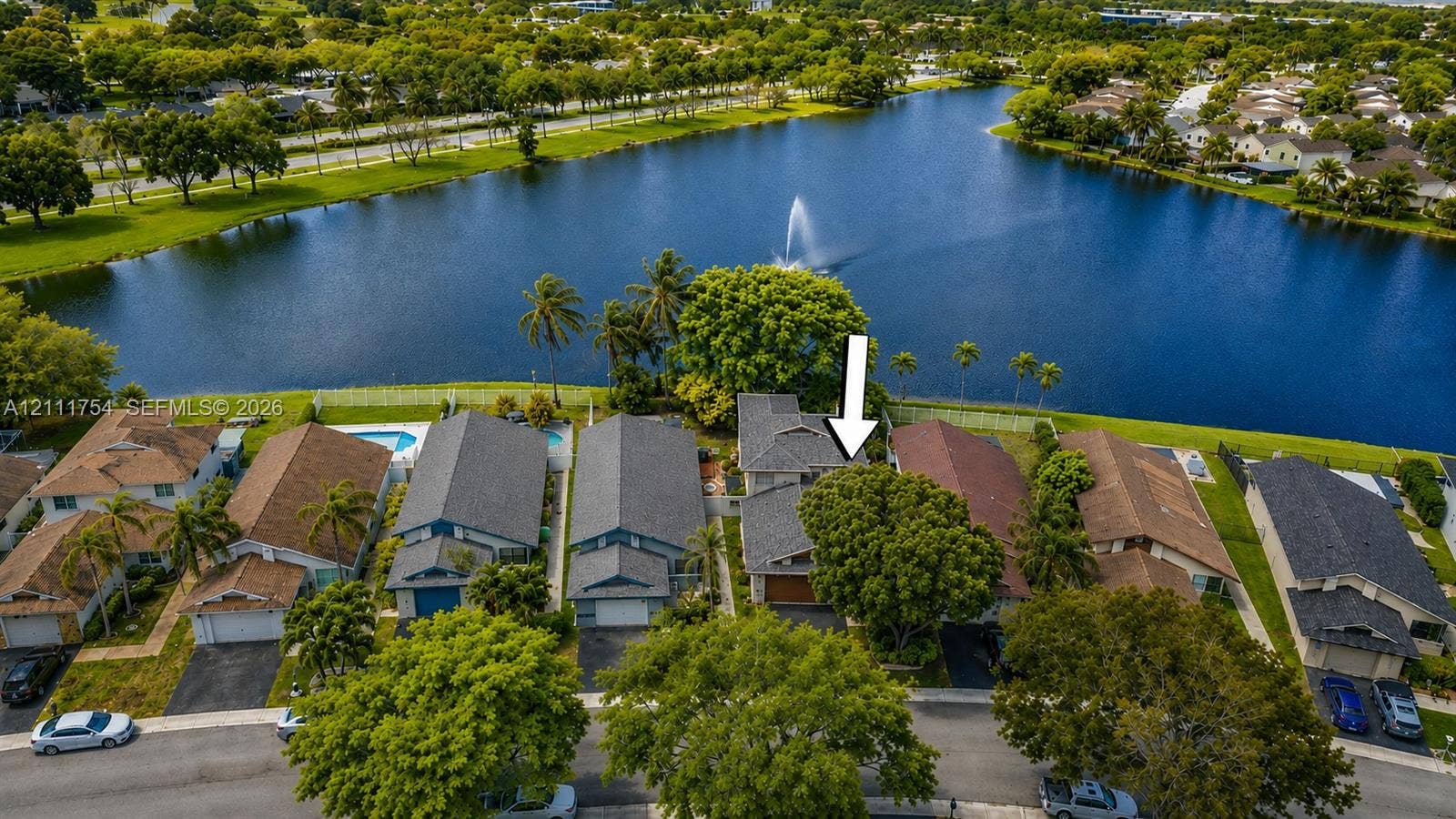 527 Lakeside Circle, Sunrise, FL 33326 Aerial perspective of the waterfront property featuring a multi-gabled roofline, asphalt shingle roofing, paved driveway, and mature landscaping