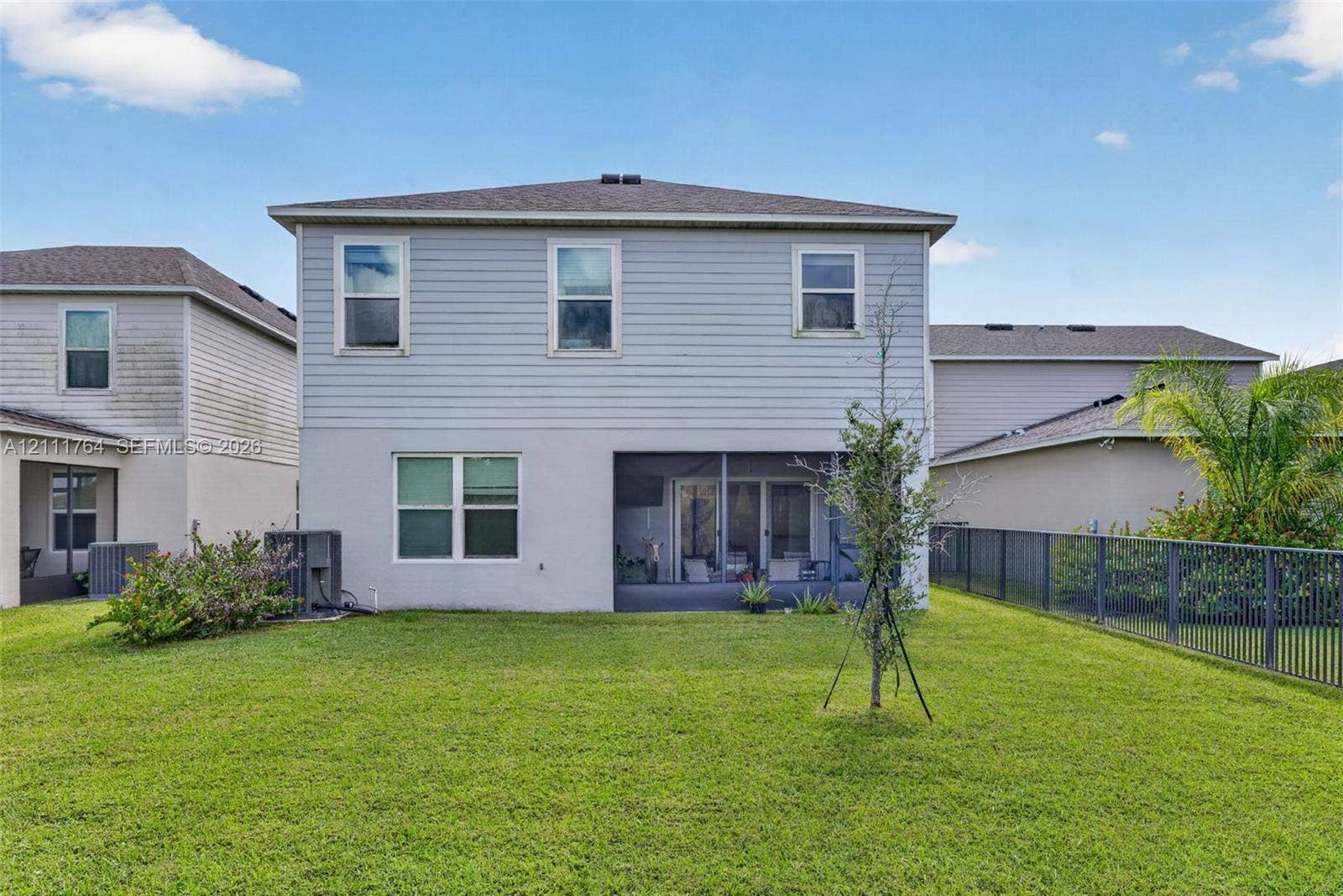 Two-story exterior featuring light-toned horizontal siding, a screened-in lanai, and an expansive grass lawn enclosed by metal fencing