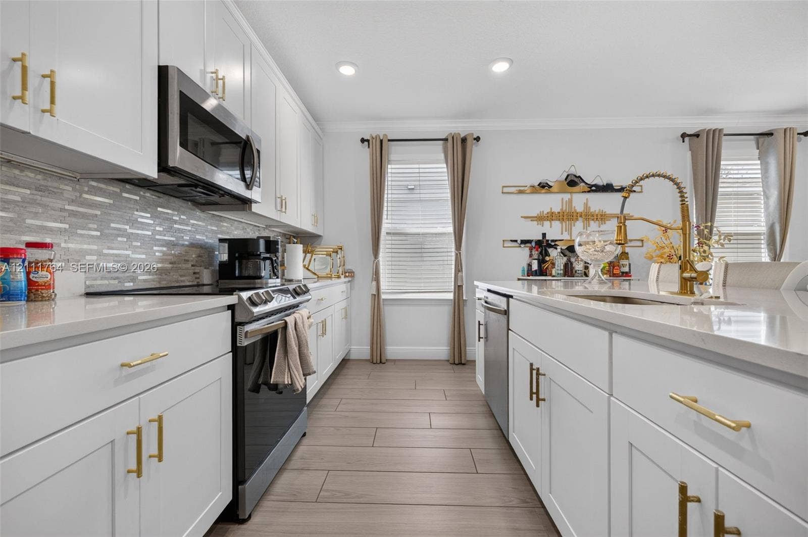 Kitchen featuring white shaker-style cabinetry, quartz countertops, stainless steel appliances, a multi-tonal linear tile backsplash, and wood-finish tile flooring