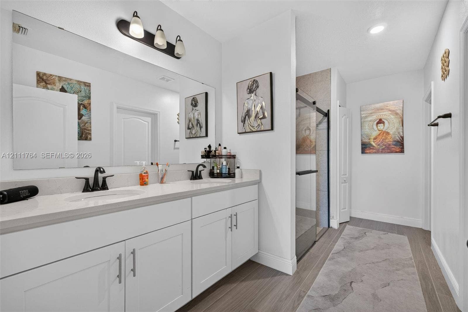 Dual-sink vanity with light-toned cabinetry, solid-surface countertop, matte black fixtures, and full-width vanity mirror