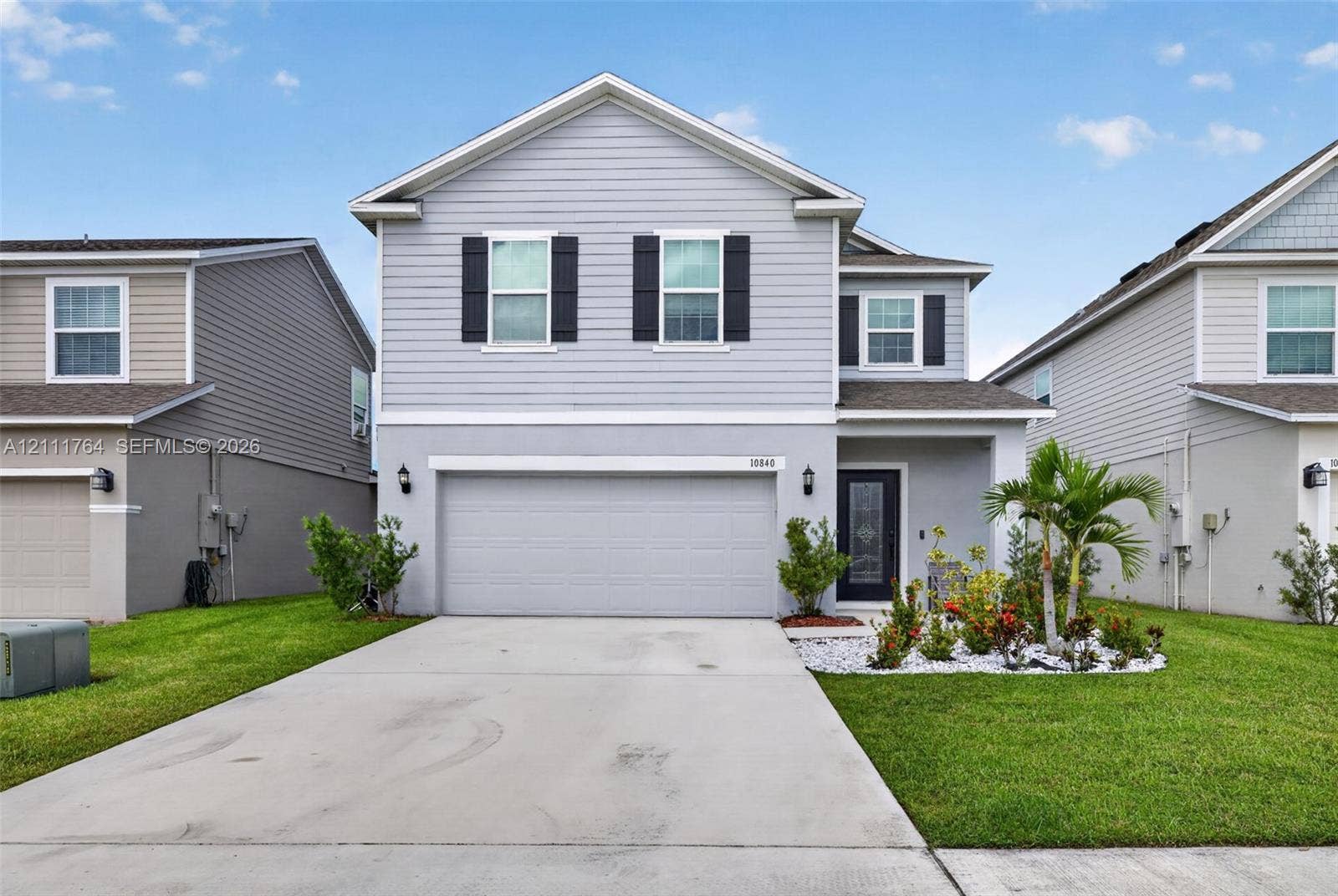 Two-story residence featuring light gray horizontal siding, dark decorative exterior shutters, a concrete driveway, and a front-facing attached two-car garage