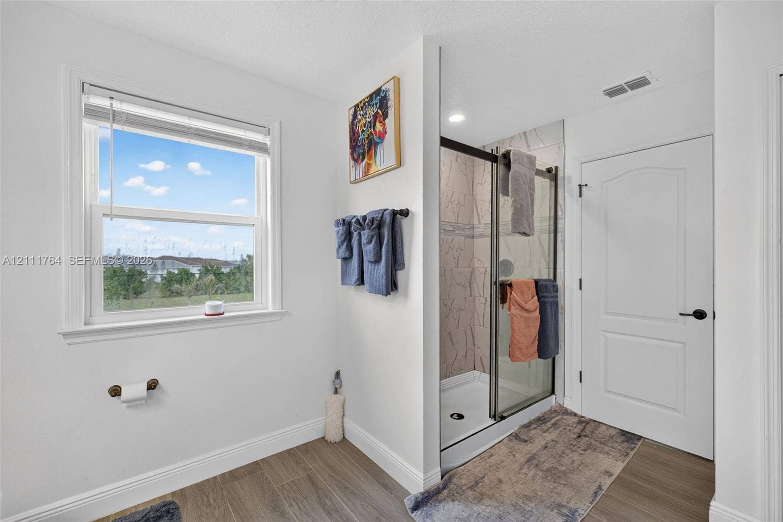 Walk-in shower with a sliding glass door, patterned tile surround, and wood-finish flooring