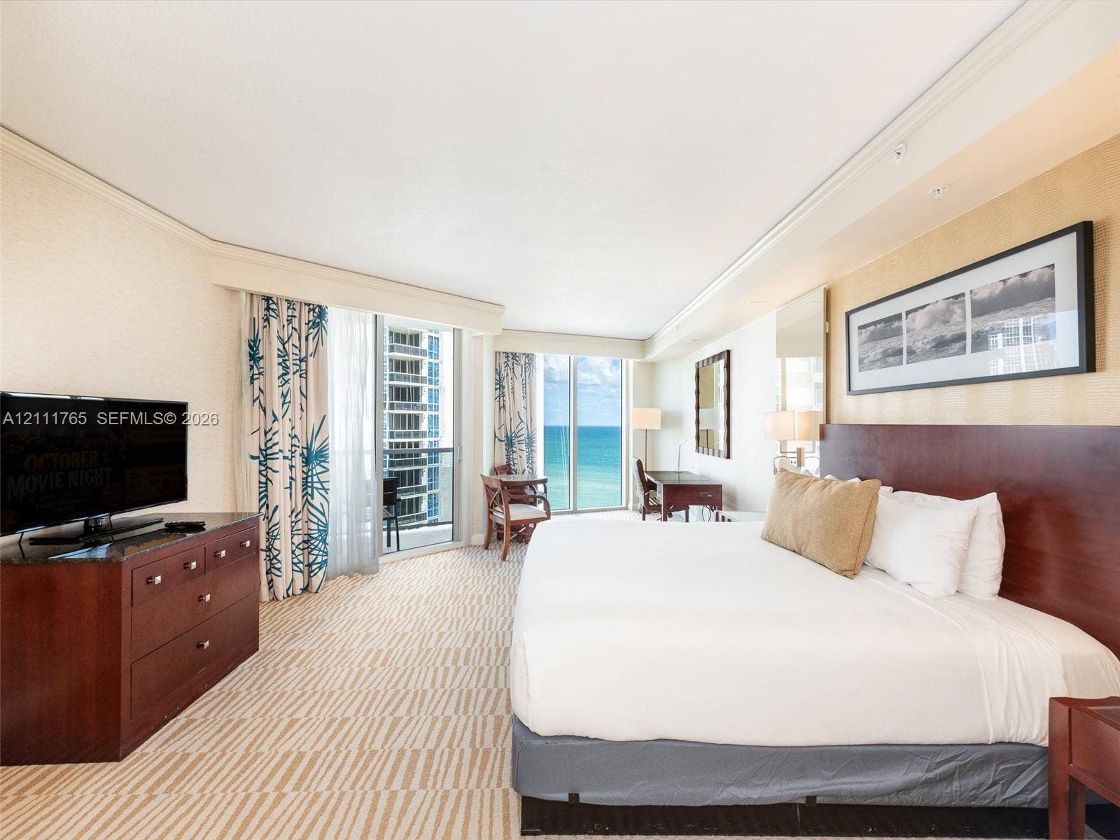 Floor-to-ceiling glass sliding doors opening to a balcony with ocean scenery, wall-to-wall patterned carpeting, and recessed ceiling lighting
