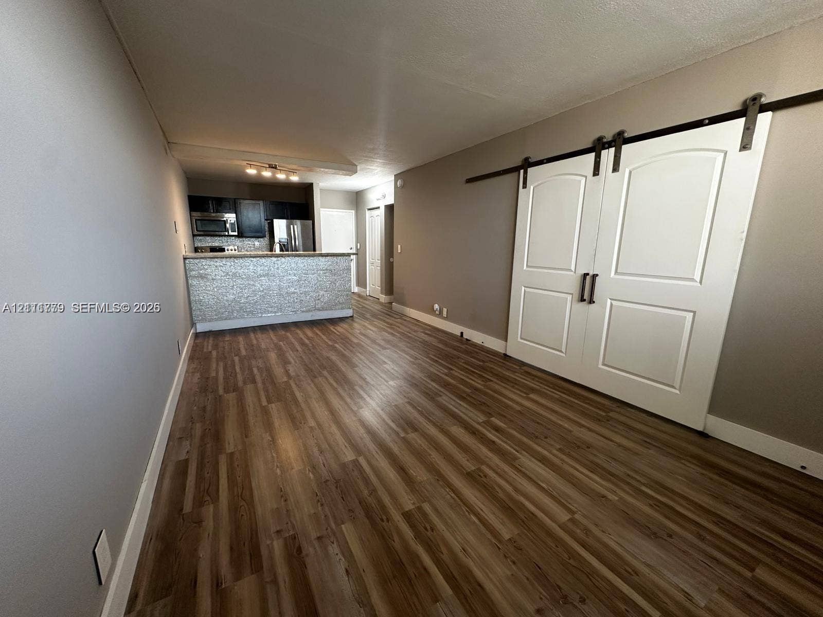 2401 Riverside Drive, #511-B, Coral Springs, Coral Springs, FL 33065 Wood-finish flooring throughout featuring double white barn doors with matte black hardware, stone-tiled breakfast bar, and stainless steel kitchen appliances