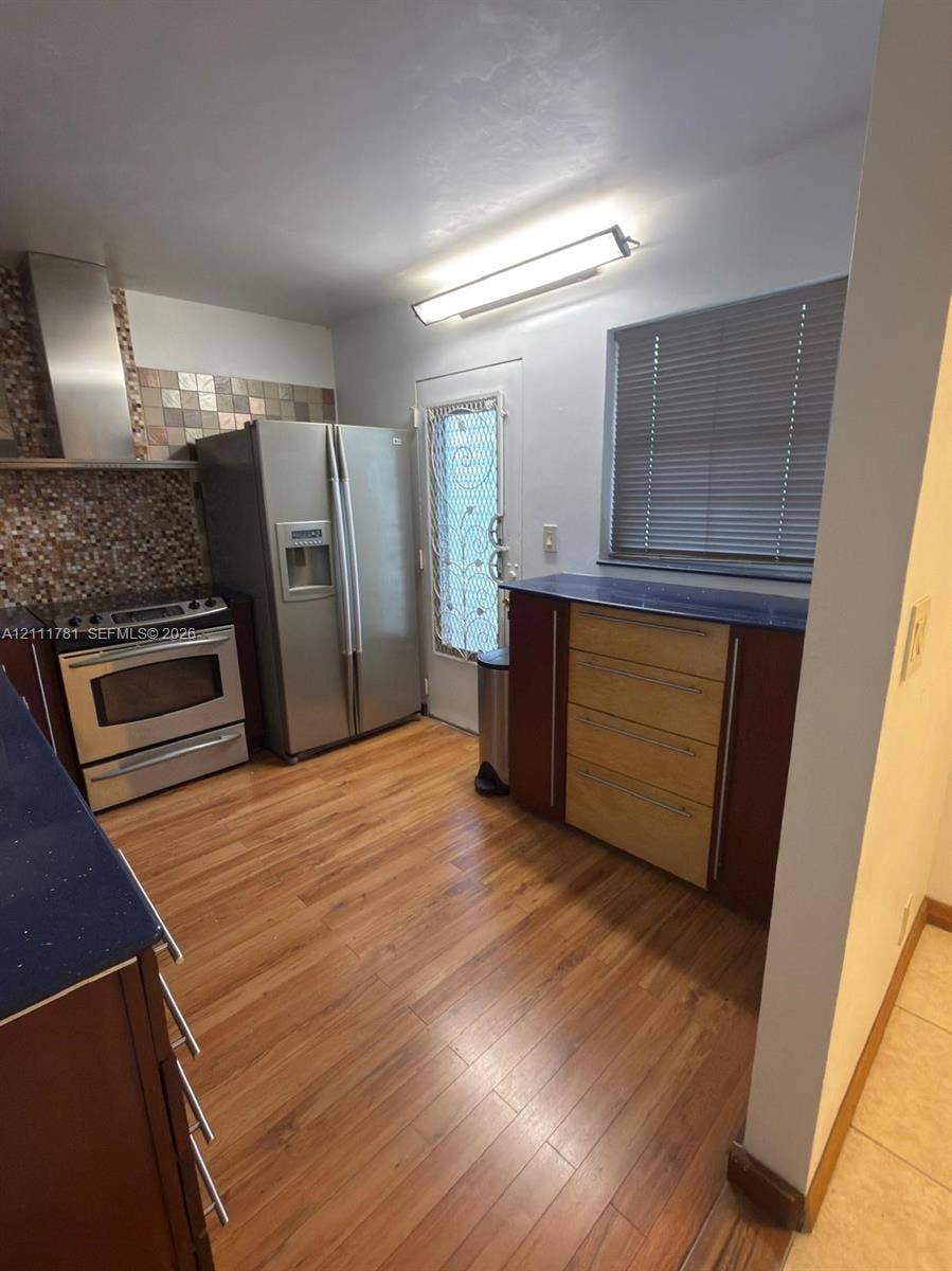 900 NE 12th Avenue, #401, Hallandale Beach, Hallandale Beach, FL 33009 Kitchen featuring wood-finish flooring, stainless steel appliances, mosaic tile backsplash, solid-surface countertops, and wood-toned cabinetry
