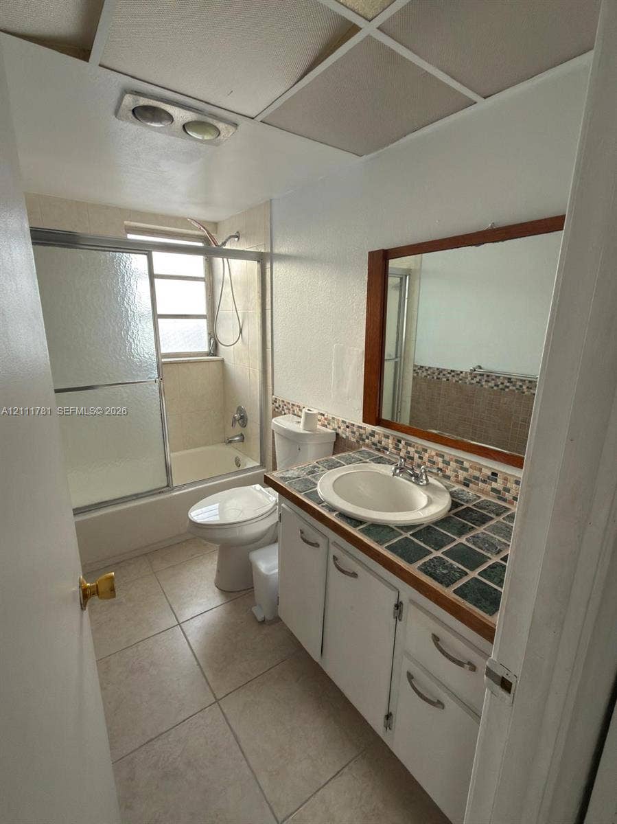 900 NE 12th Avenue, #401, Hallandale Beach, Hallandale Beach, FL 33009 Bathroom featuring a vanity with a tiled countertop, drop-in sink, framed mirror, and a tub-shower combination with a sliding glass enclosure
