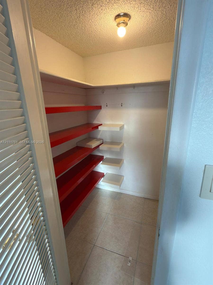 900 NE 12th Avenue, #401, Hallandale Beach, Hallandale Beach, FL 33009 Storage closet featuring tile flooring, louvered door, overhead flush-mount lighting, and multi-level wall-mounted shelving