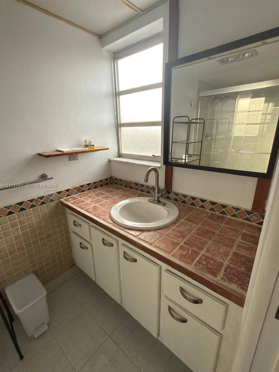 900 NE 12th Avenue, #401, Hallandale Beach, Hallandale Beach, FL 33009 Vanity featuring a tiled countertop with decorative trim, an integrated circular sink, polished metal faucet, and white cabinetry