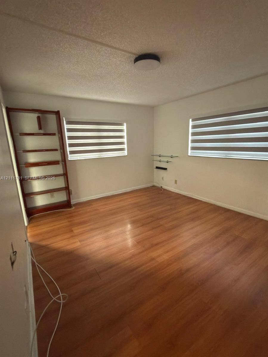 900 NE 12th Avenue, #401, Hallandale Beach, Hallandale Beach, FL 33009 Room featuring wood-finish flooring, dual windows with fitted light-filtering shades, a built-in wooden shelving unit, and a central flush-mount ceiling fixture