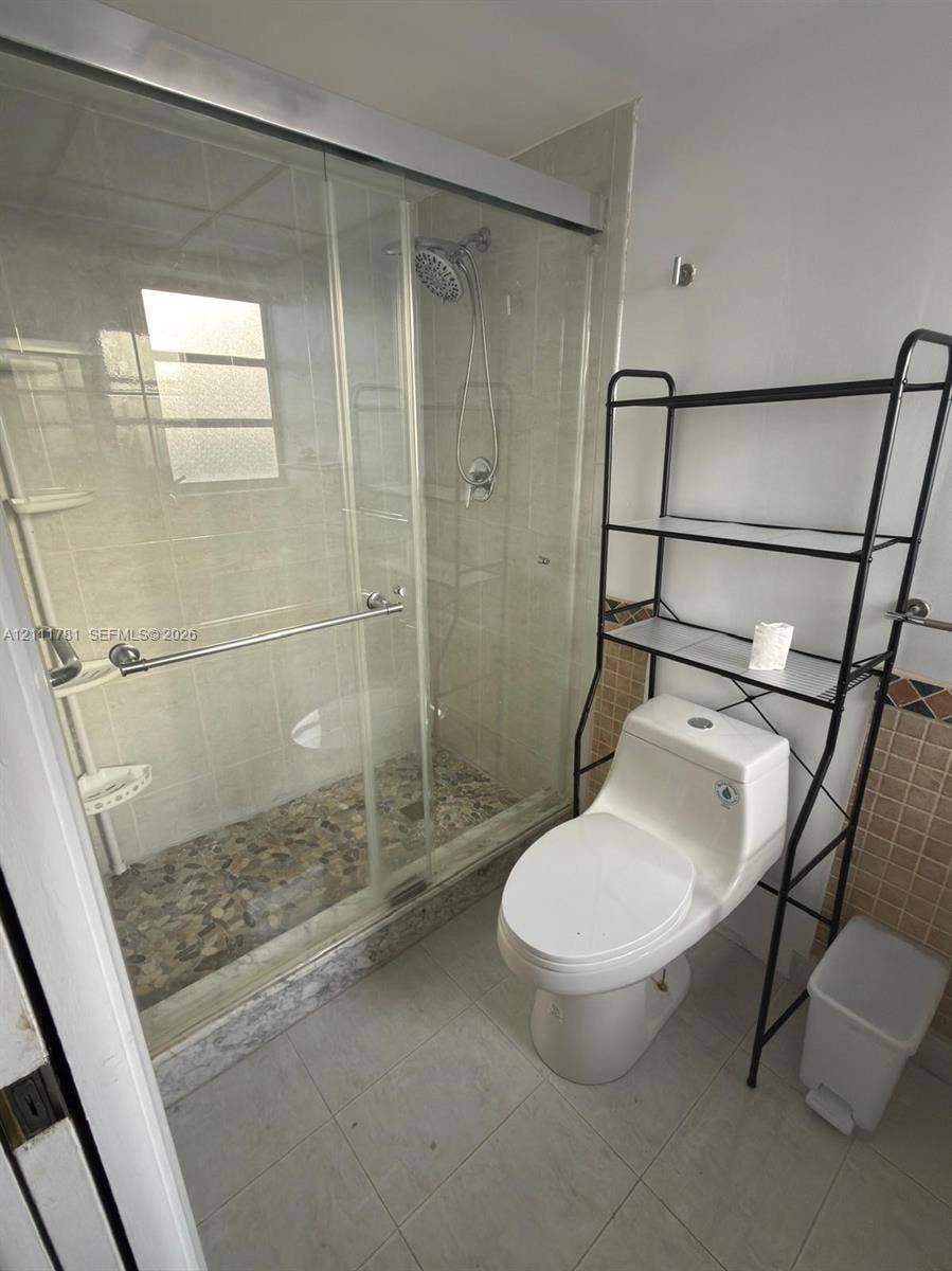 900 NE 12th Avenue, #401, Hallandale Beach, Hallandale Beach, FL 33009 Walk-in shower featuring a sliding glass enclosure, pebble-stone flooring, and a wall-mounted showerhead, complemented by a dual-flush toilet and neutral tile wall accents