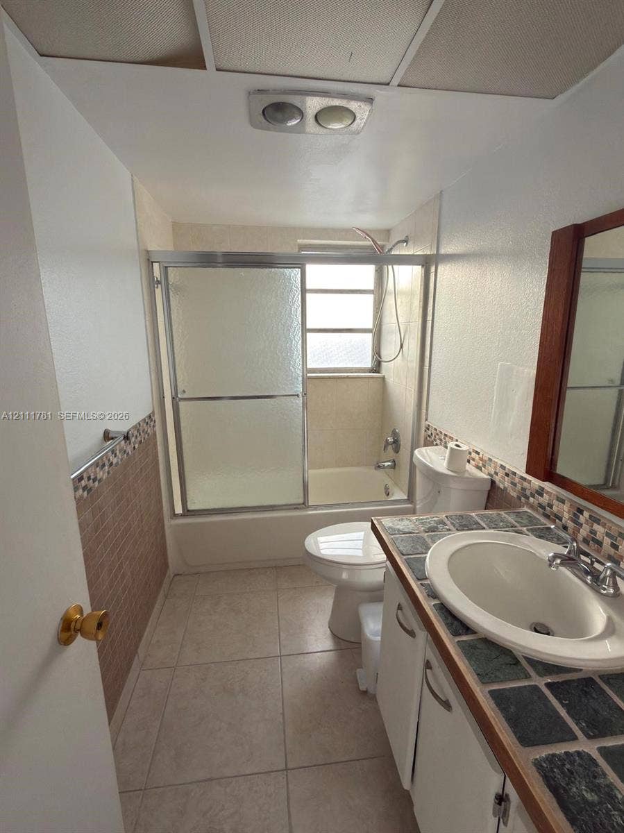 900 NE 12th Avenue, #401, Hallandale Beach, Hallandale Beach, FL 33009 Bathroom featuring a tub-shower combination with sliding glass doors, tile-topped vanity with an integrated basin, tile flooring, and decorative mosaic wall tile accents