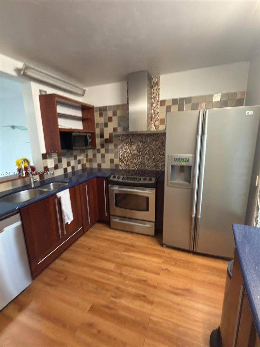 900 NE 12th Avenue, #401, Hallandale Beach, Hallandale Beach, FL 33009 Kitchen featuring dark-toned cabinetry, stainless steel appliances, a chimney-style range hood, decorative tile backsplash, and wood-finish flooring
