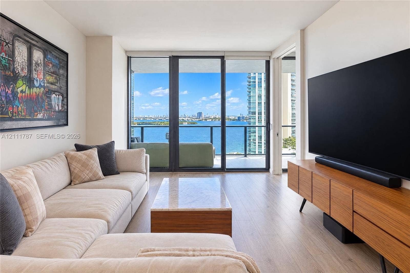 Floor-to-ceiling glass sliding doors, wood-finish flooring, and a private balcony featuring a water backdrop