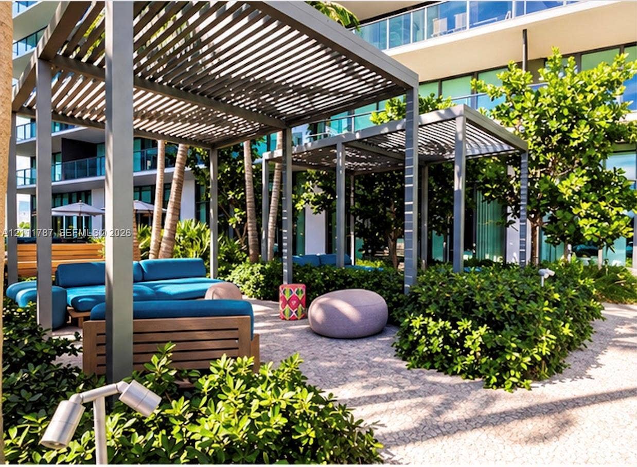 Outdoor lounge area featuring dual metal pergolas, stone paver flooring, integrated landscaping, and privacy shrubbery