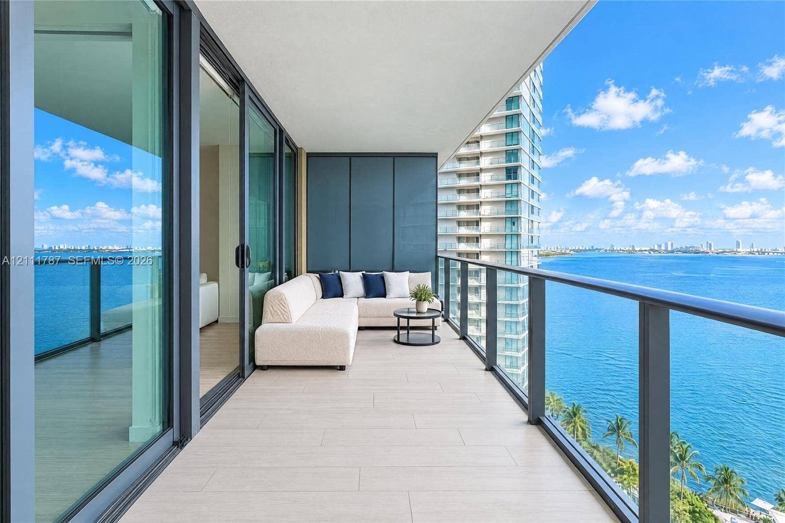 Covered balcony featuring tile flooring, full-height glass sliding doors, and a dark metal railing, accented by opaque privacy paneling