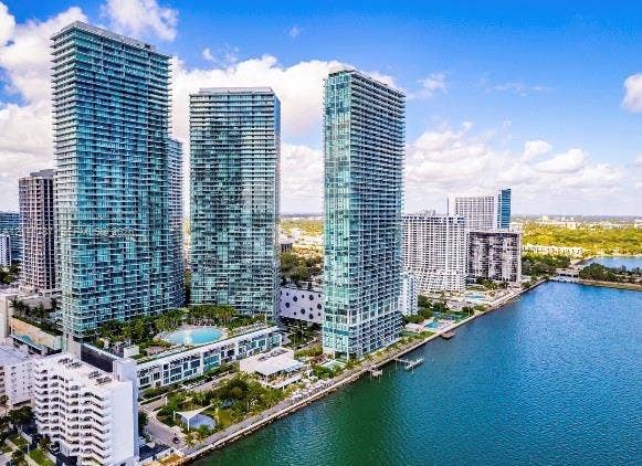 High-rise towers featuring glass-paneled balconies, floor-to-ceiling windows, and a waterfront location with an outdoor swimming pool