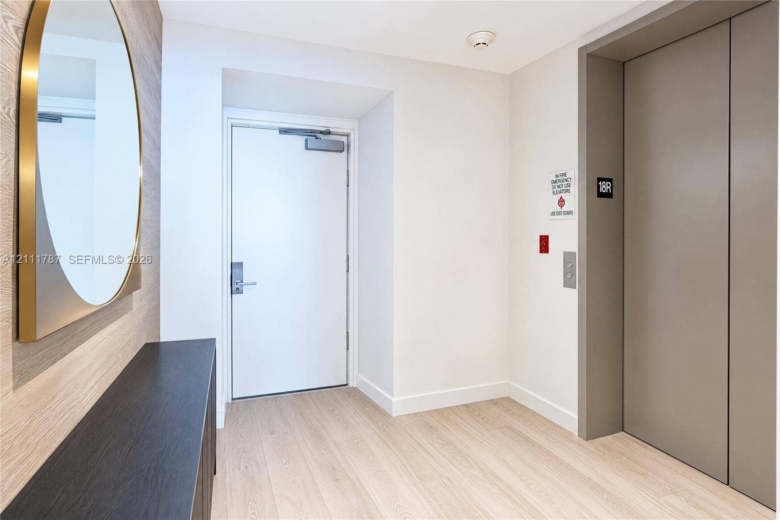 Elevator landing area featuring wood-finish flooring, a built-in dark wood-tone console, and an arched mirror with a gold-tone frame